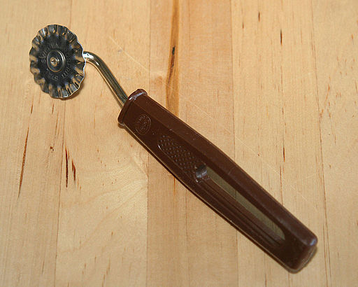 image of a pastry wheel. A brown plastic handle with a metal wheel that is ridged in the ends.