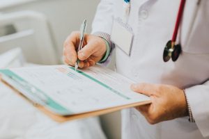 A doctor writing patient information on a form and clipboard
