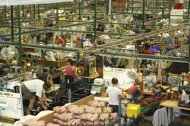 Workers on the floor of a factory all doing individual tasks.