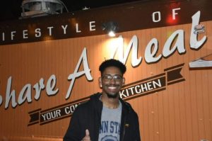 Young man standing in front of a sign that reads "Share a Meal"