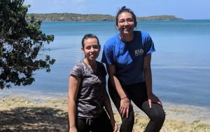 Two women smiling into camera standing on the banks of a lake