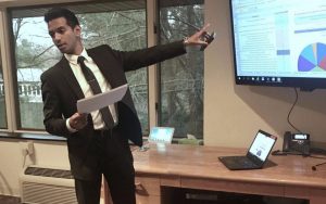 Young professional in a suit pointing to an image on a TV screen