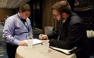 Older man in suit pointing out something on a piece of paper to a younger man in a dress shirt