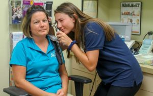 Young woman using medical instrument to examine inside the ear of a female patient.