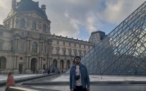 Young man standing outside of the Louvre Museum in Paris.