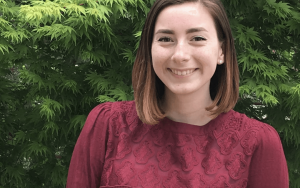 Young woman in maroon shirt standing in front of greenery