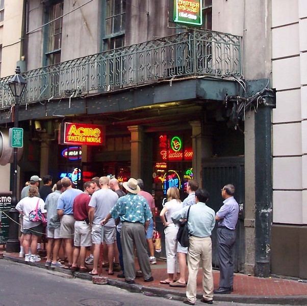 A long line of people stand on the sidewalk in front of a restaurant waiting to get in.