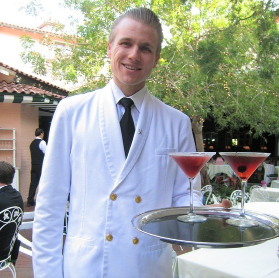 A smiling waiter delivering cocktails on a tray.