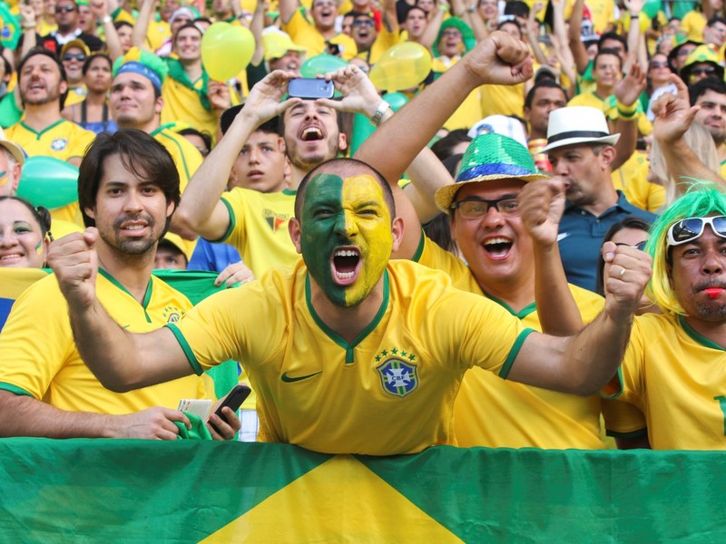 Brazilian soccer fans dressed in the colors of the national team cheer wildly from the stands during a match.
