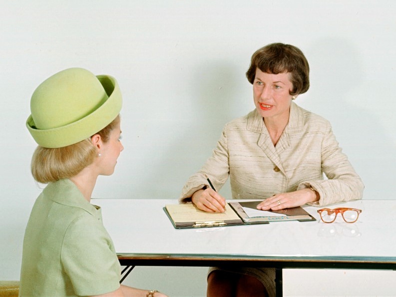 Two women sit across a table from one another during a job interview.