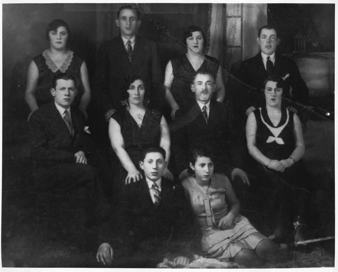 Black and white photo of four individuals standing at the back, four individuals seated in the middle row on chairs and two individuals seated on the floor at the front.