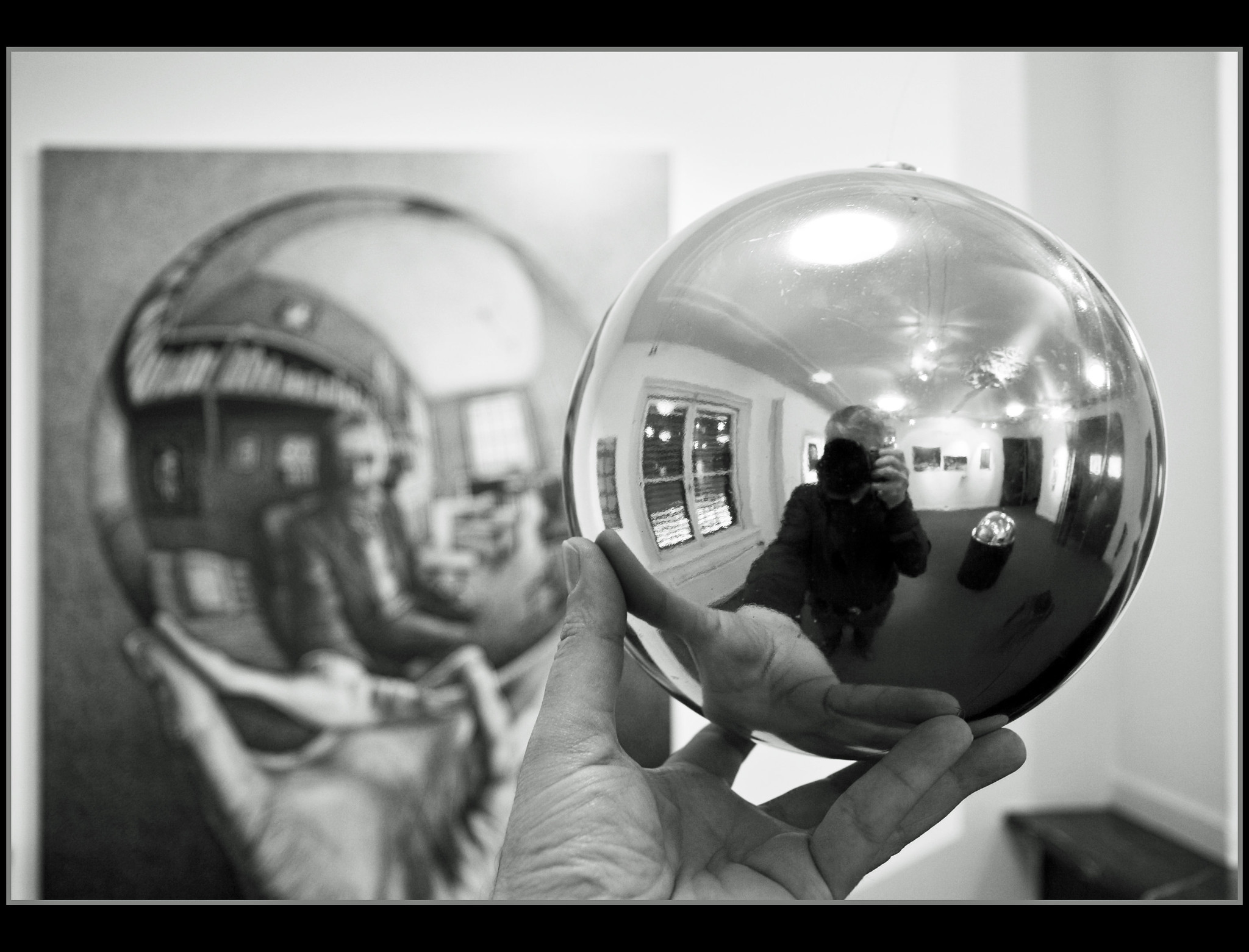 The reflection of the author taking a picture of a chrome ball with Escher's similar artwork in the background