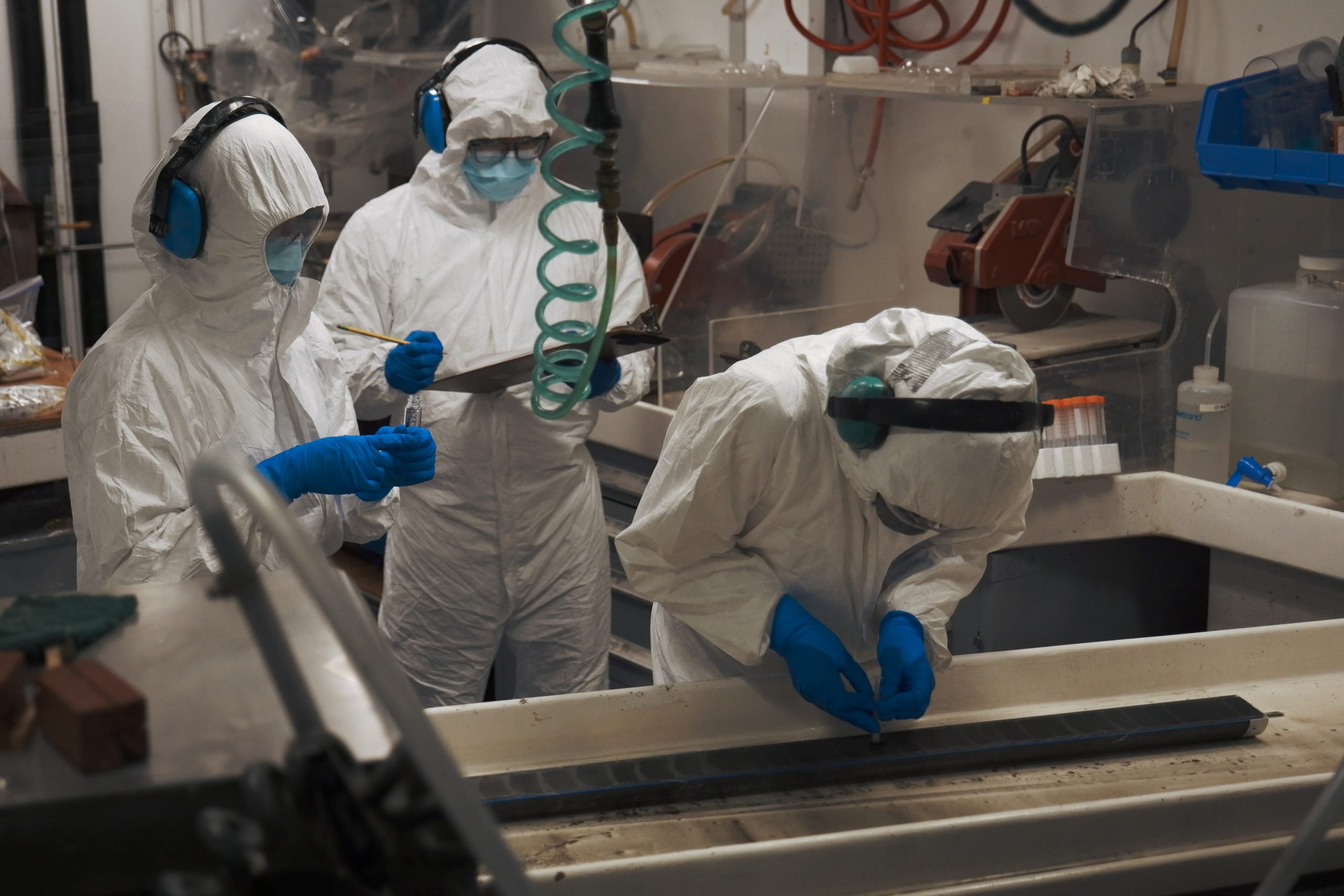 Three people in white safety suits in a laboratory looking at a core of deep sea material
