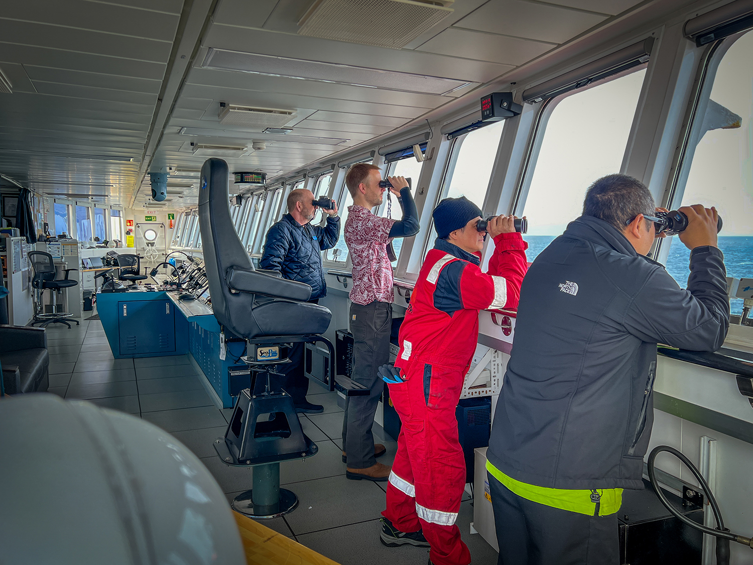 four people looking through a ship window with binoculars