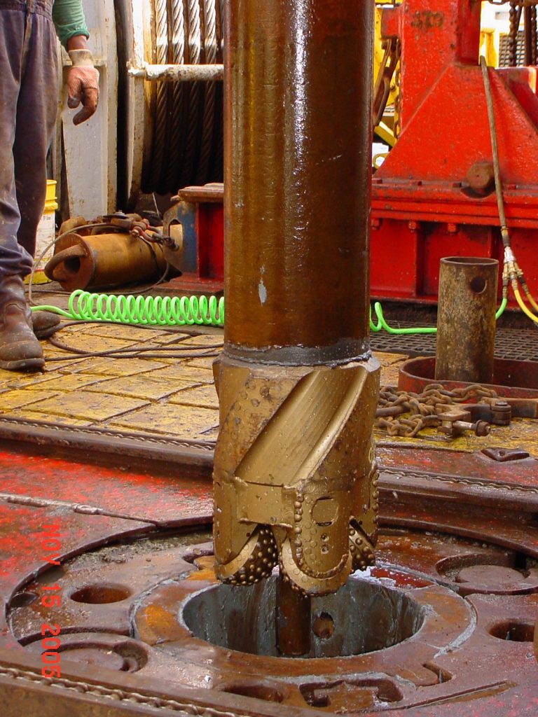 drill bit attached to a pipe about to be lowered through the deck of a ship