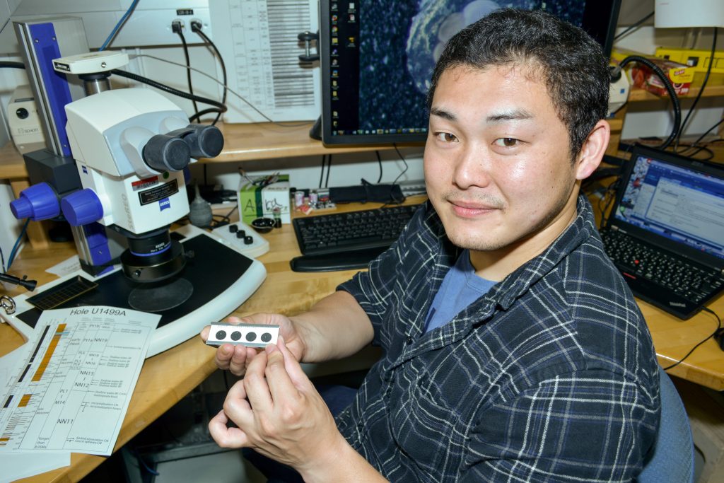 person sitting at microscope holding microscope slide