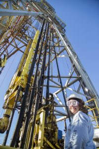 Person standing at base of drilling tower wearing safety glasses and hard hat