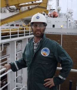 Person standing on a ship wearing a hardhat and work coveralls