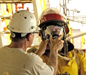 Person wearing white hardhat helping another person put on emergency fire protection mask