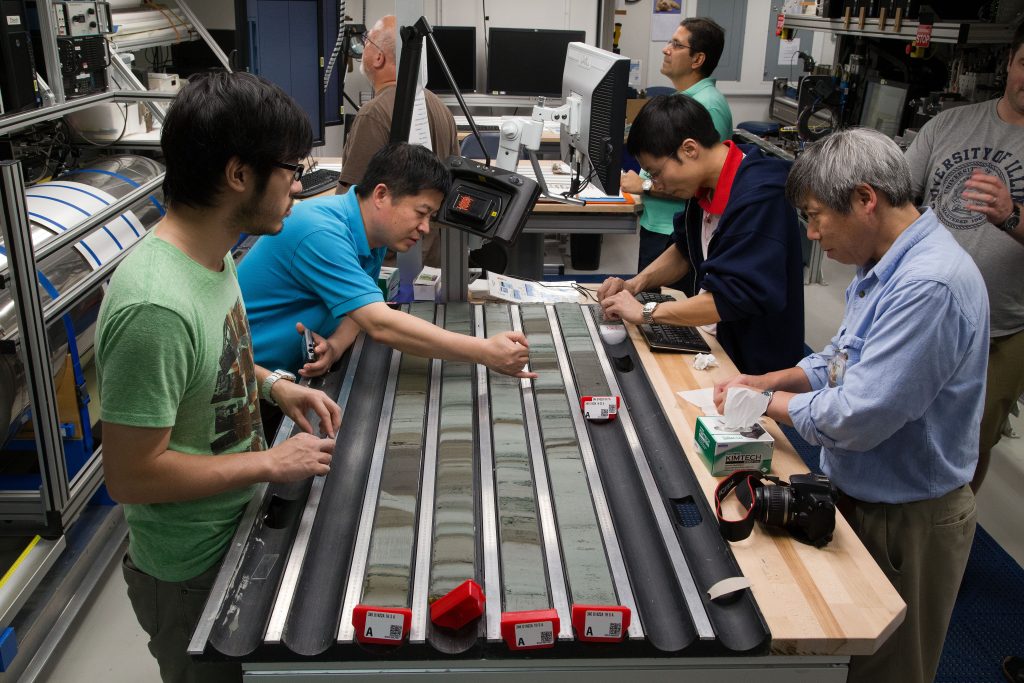 Four scientists standing around a table looking at four samples of split sediment core