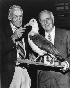 Two smiling men standing with a stuffed albatross.