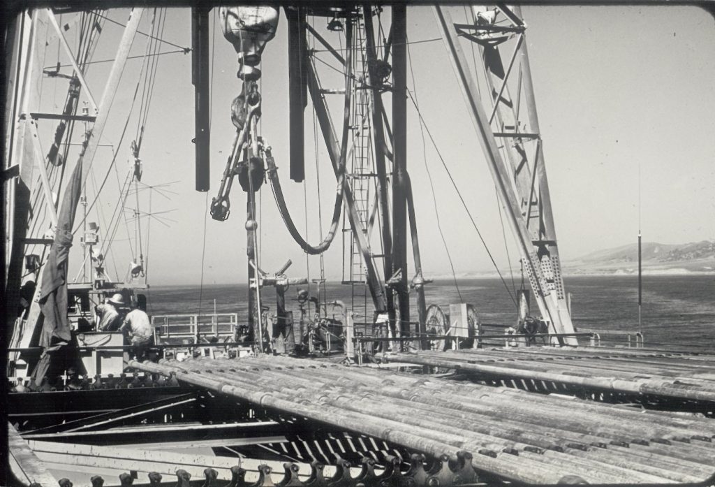 rows of horizontal pipes on the back of the ship, with the lower part of a drilling derrick present in the photo