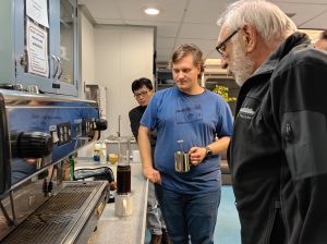 Three people starting at a coffee press and expresso machine