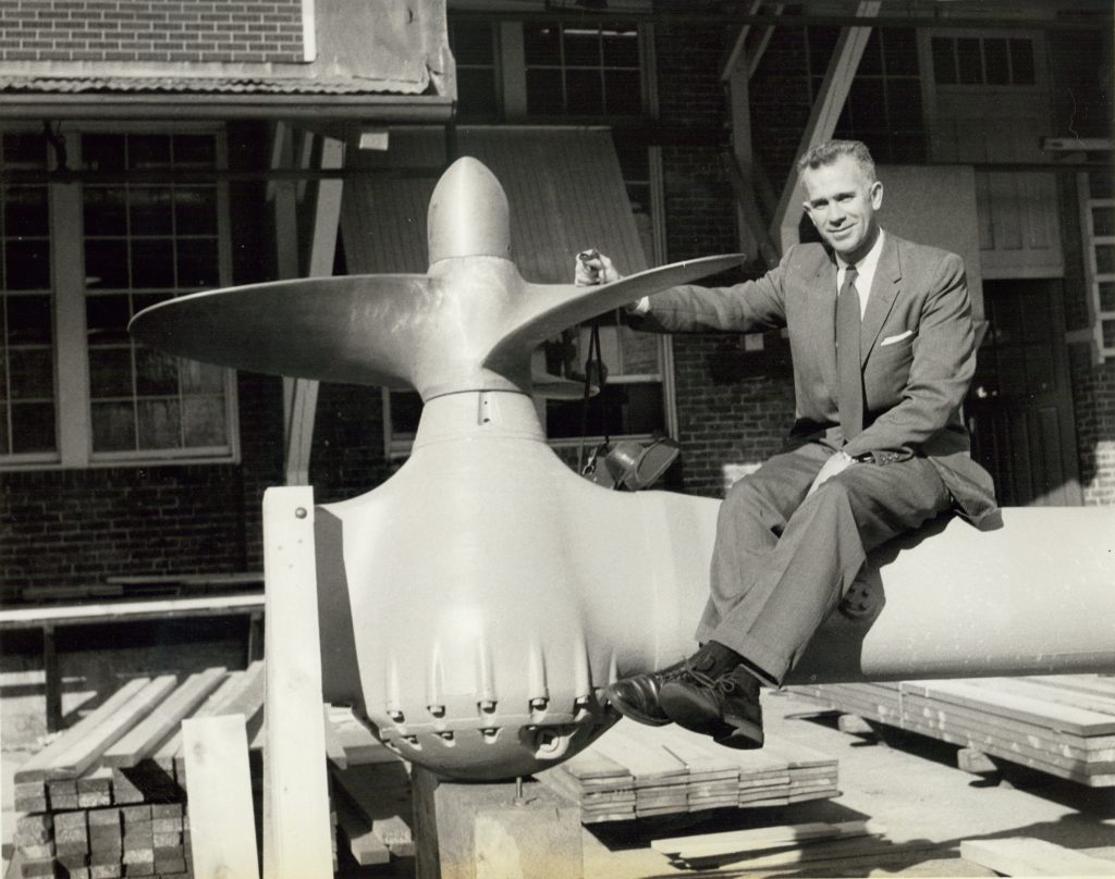 Man in a suit sitting on top of a ship propeller