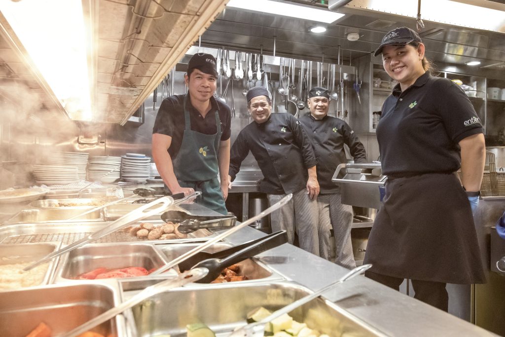 Four chefs in a kitchen looking over a buffet of food