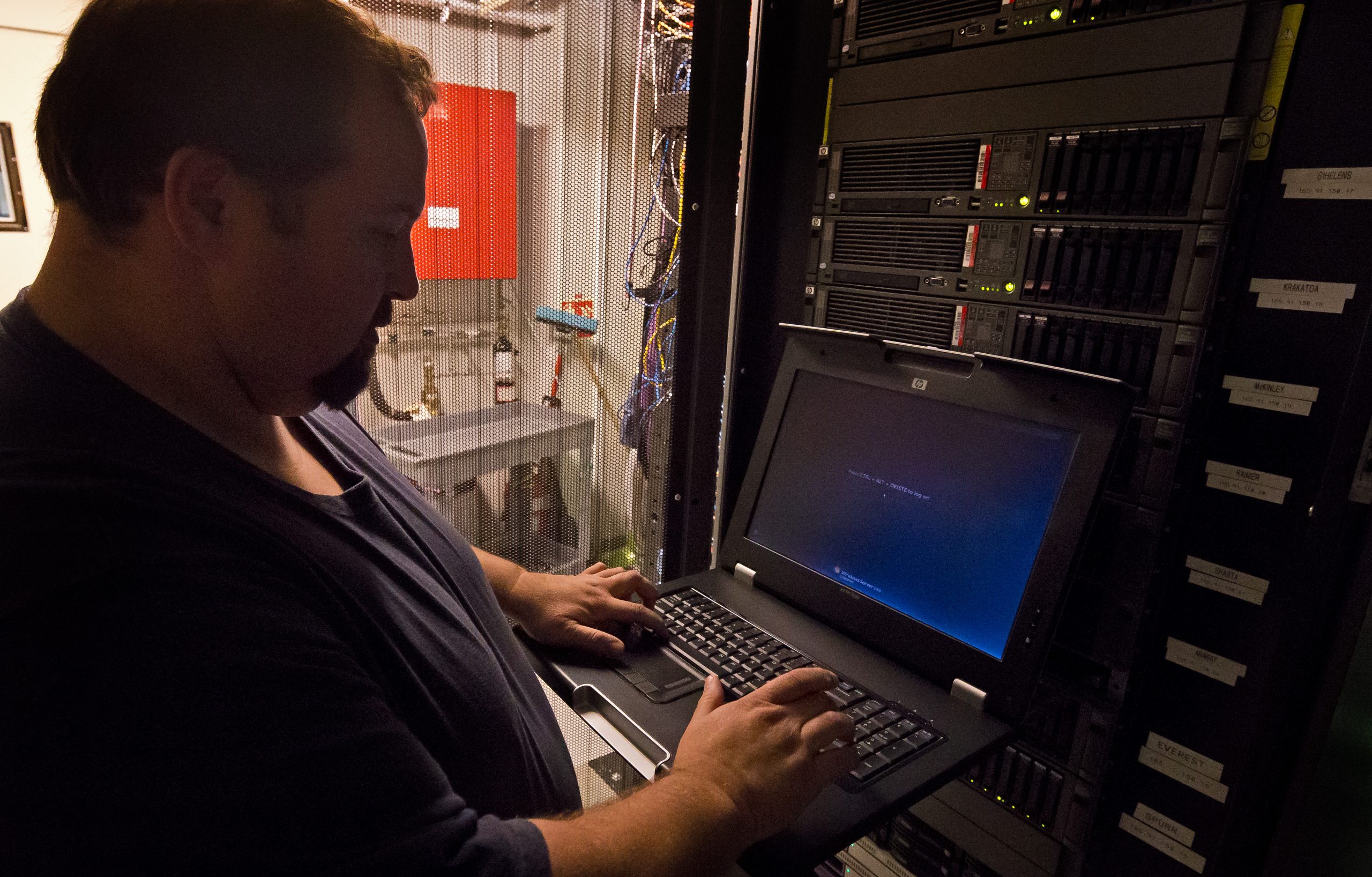 Man facing an open laptop in a computer server room.