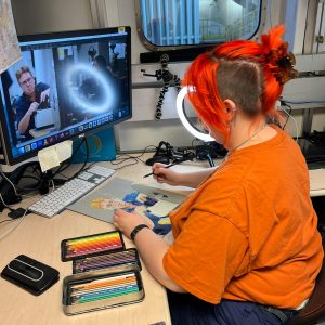 person sitting and looking at an image on a computer screen while sketching