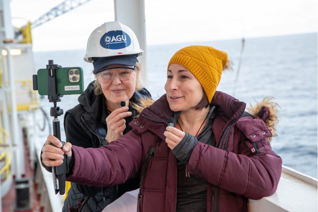 Two people on a ship looking and talking at a cell phone