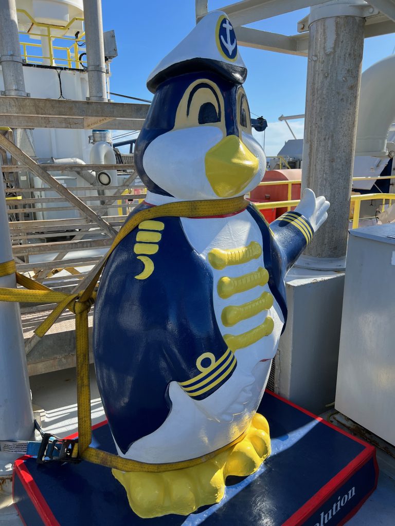 Penguin statue on a ship dressed in a sailor's suit in the colors of blue, white, and yellow