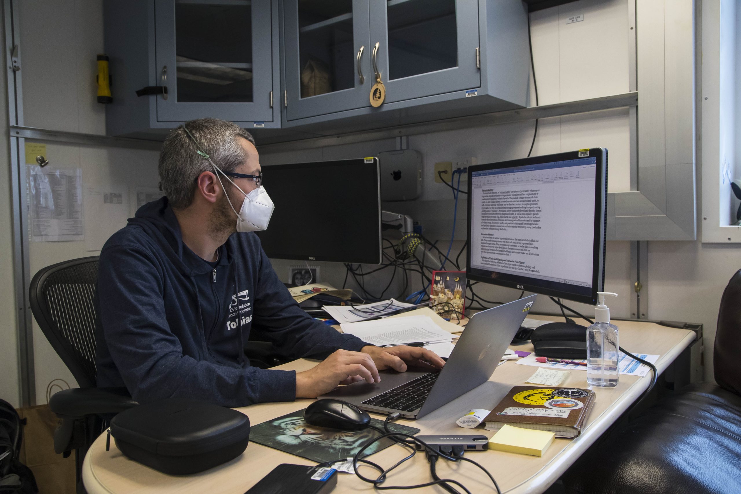 Person wearing a mask typing at a computer