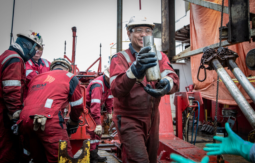 A Siem crewmember hands off the core catcher to an IODP staff member waiting on the catwalk (Credit: Erick Bravo, IODP JRSO, MerlinOne Photo Archive, CC BY 4.0).