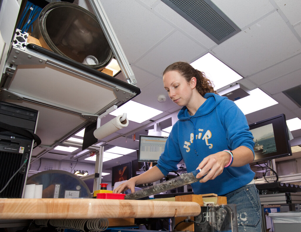 Woman in a blue sweatshirt is handling a rock core.